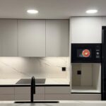 Proyecto de reforma de cocina en Barcelona con diseño contemporáneo, península, acabados claros, detalles negros y una distribución conectada con el salón.