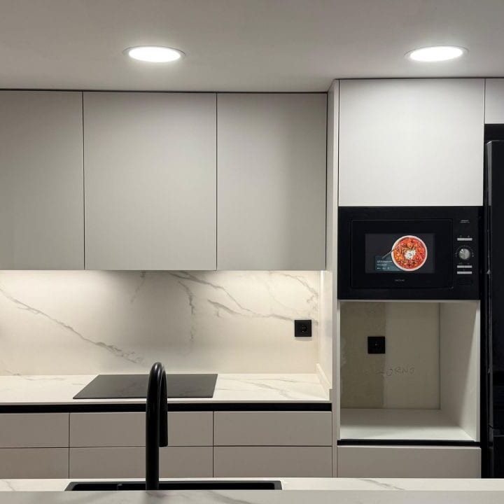 Proyecto de reforma de cocina en Barcelona con diseño contemporáneo, península, acabados claros, detalles negros y una distribución conectada con el salón.