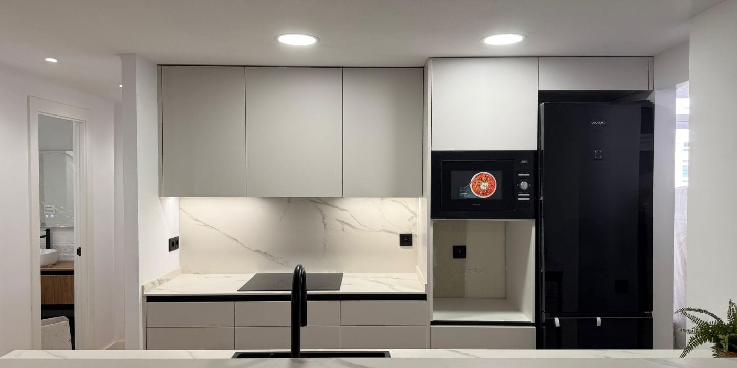 Proyecto de reforma de cocina en Barcelona con diseño contemporáneo, península, acabados claros, detalles negros y una distribución conectada con el salón.